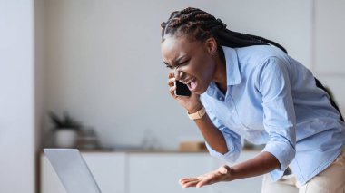 İşteki sorunlar. Stresli siyahi iş kadını cep telefonuyla konuşuyor ve bağırıyor, dizüstü bilgisayar programında sorunları var, boş yer var.