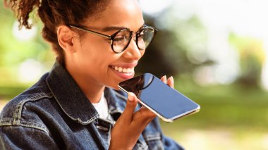 Açık havada oturan hoparlör modu kullanarak akıllı telefonlu siyah kadın arama yapıyor. Modern İletişim. Panorama