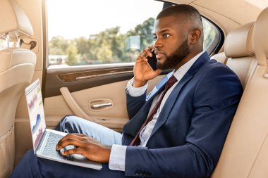 Zengin, yakışıklı afro-amerikan işadamı, şık takım elbiseli, arabada çalışıyor, dizüstü bilgisayar kullanıyor ve akıllı telefonla konuşuyor, internette çalışıyor, kopyalama alanında çalışıyor. Yoğunlaştırılmış siyah yönetici telefon görüşmesi yapıyor, yan görünüm