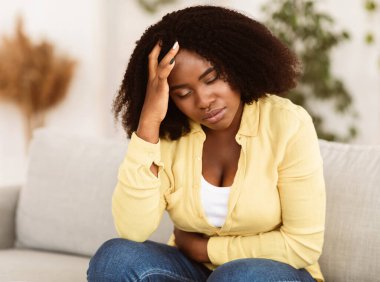 Üzgün siyah kadın adet sancısı ve adet sancısı çekiyor. Mide ağrısı, karın ağrısı ve baş ağrısı.