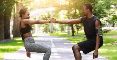 Spor 'da takım çalışması. Aktif siyah çift şehir parkında birlikte egzersiz yapıyor, birbirlerine destek oluyor, eş eğitimi alıyor, boş alan yaratıyor.