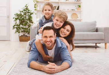 Komik Aile Portresi. Mutlu ebeveynler ve çocuklar evde kameraya bakarak yerde birlikte poz veriyorlar. Boş Alan