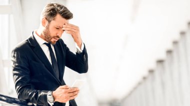 Havaalanı terminalinin penceresinde duran yorgun işadamı cep telefonu kullanıyor, alnına dokunuyor, baş ağrısı çekiyor, kopyalama alanı kullanıyor. Girişimcinin iş sorunları var, akıllı telefondan e-postaları okuyor