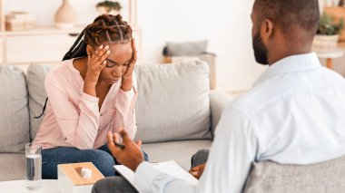 Bireysel psikoterapi. Depresyondaki siyahi kadın danışmanlık ofisinde kanepede oturuyor, sorunlarını paylaşıyor, doktorla hastayla konuşuyor.