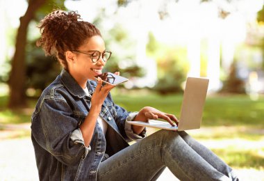 Cep telefonu hoparlörüyle konuşan siyahi Freelancer Kız dışarıda dizüstü bilgisayarla çalışıyor. Serbest Kariyer Konsepti