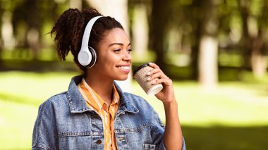 Neşeli siyahi kadın kahve içiyor. Kulaklıkla müzik dinliyor. Şehir parkında yürüyor. Hafta sonunun tadını çıkarmak, Sonbahar Yürüyüş Çalma Listesi. Panorama