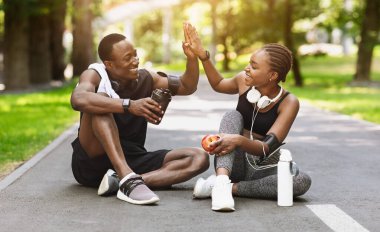 İlişki Hedefleri. Başarılı açık hava eğitiminden sonra aktif Afrikalı çift, parkta dinlenirken birbirlerine beşlik çakıyor.