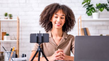 Müritler ve öğrenciler için podcast ve webinar. Gülümseyen Afrikalı Amerikalı kadın akıllı telefonuyla web kamerasına bakıyor.