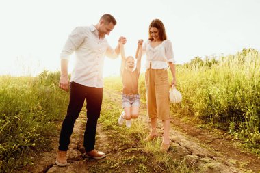 Mutlu anlar. Genç ebeveynler bebeklerini elleriyle tutuyorlar ve zıplamasına yardım ediyorlar.