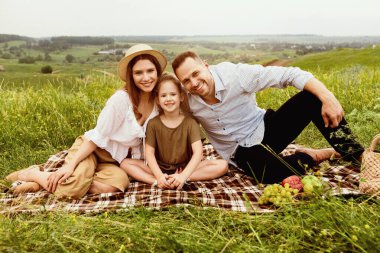 Bağlanma kavramı. Neşeli aile dışarıda pikniğin tadını çıkarıyor, battaniyeye oturup kameraya bakıyor, boş alan arıyor.