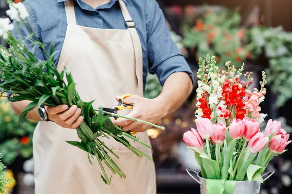 Küçük işletme, çiçek tasarım stüdyosu, buket üretimi, covid-19 sırasında çiçek teslimatı, sipariş oluşturma. Önlüklü milenyum erkek çiçekçisi kompozisyon, kırpılmış, boş alan için bitkileri buduyor