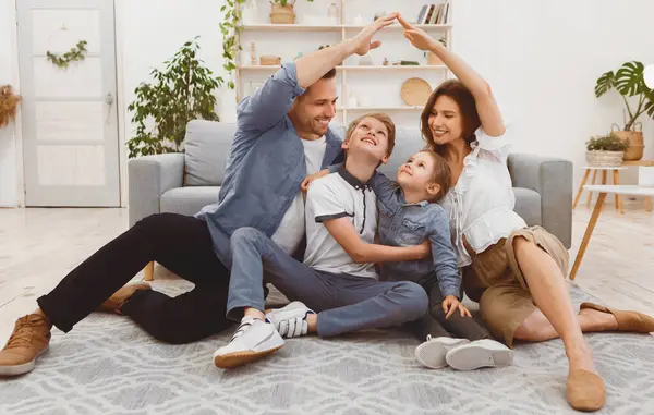 Aile için konut. Genç ebeveynler el ele tutuşuyor sembolik ev çatısı yapıyorlar. Çocuklarla birlikte yeni dairede oturuyorlar..