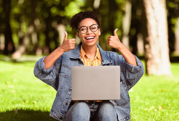 Dizüstü bilgisayarlı siyahi kadın başparmaklarını kaldırarak şehir parkında çalışıyor. Harika Web Sitesi Kavramı