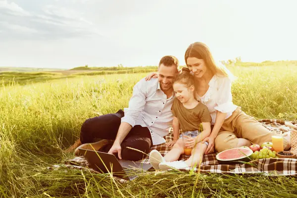 Mutlu sevgi dolu aile pikniğin tadını çıkarıyor, battaniyeye oturuyor ve dizüstü bilgisayar kullanıyor, boşluğu kopyalıyor.