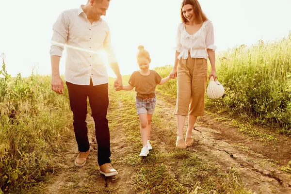 Bir çocukla zaman geçirmek. Mutlu bebek çayırda yürüyor ve gün batımında anne ve babasını elleriyle tutuyor.