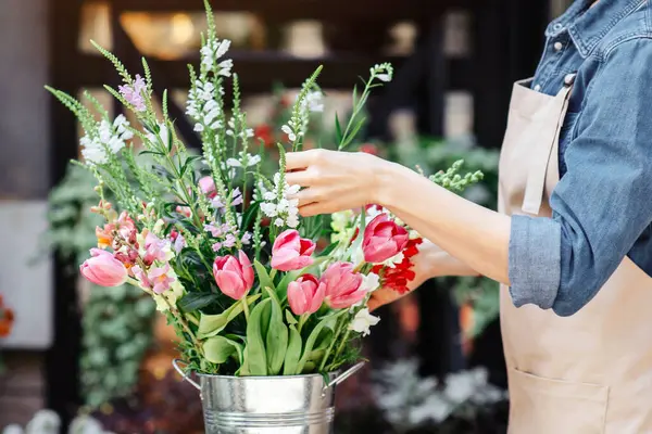COVID-19 tecridi sırasında sosyal mesafe ve modern hizmet. Önlüklü ve koruyucu maskeli çekici, genç, dost canlısı bayan müşteri için çiçekçi profili hazırlıyor.
