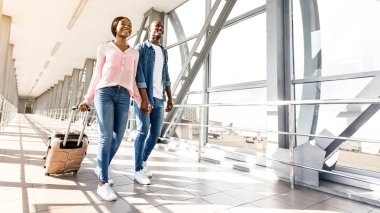 Tatil gezisi. Romantik Afrikalı çift bavullarıyla havaalanının kapısına yürüyorlar, bavullarıyla yürüyorlar ve kucaklaşıyorlar.