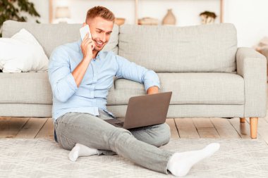 İçişleri Bakanlığı Konsepti. Cep telefonuyla konuşan genç adam dizüstü bilgisayarla yerde oturuyor. Boş alan