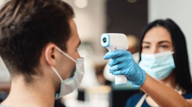 Yeni hayat kuralları. Berber dükkanında müşterinin vücut ısısını ölçen kuaför.