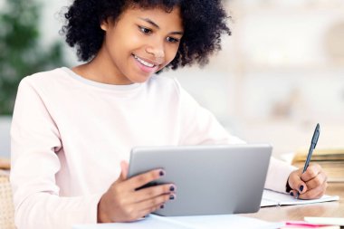 Dijital tabletli neşeli kız ödevlerini internette yapıyor. Masasında oturuyor. Uzak E-Öğrenme Konsepti