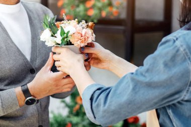 Coronavirus salgını sırasında buket ve modern servis satın almak ve yeni normaller. Genç bayan satıcı ya da önlüklü ve koruyucu maskeli sahibi çiçekçi, açık hava, boş yer yakınlarındaki müşterilerine sipariş veriyor.