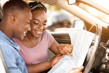 Hevesli siyah çift birlikte araba gezisi yaparken harita okuyorlar, yolun ortasında kayboluyorlar, yan manzara, kopyalama alanı. Gülümseyen Afrikalı Amerikalı genç adam ve kadın yeni bir hedef arıyorlar.