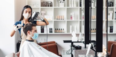 Yeni normal. Berber erkek müşteri için saç yapıyor, hem tıbbi maskeli, hem de boş alanda.