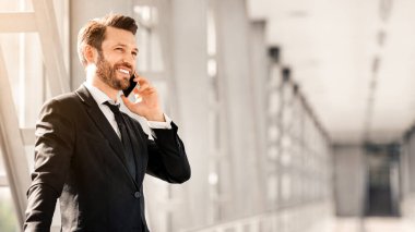 Yakışıklı orta yaşlı iş adamı havaalanında kalkışı beklerken telefonla konuşuyor, fotokopi alanına bakıyor ve gülümsüyor. Takım elbiseli mutlu bir adam akıllı telefondan iş ortaklarıyla konuşuyor.
