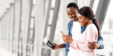 Havalimanı Terminali 'nde akıllı telefon kullanan mutlu Afrikalı çift yurt dışına uçmadan önce internet üzerinden otel rezervasyonu yapan genç siyah eşler internetten yer ayırtıyor.