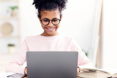 E-öğrenme. Mutlu Afrikalı genç kız laptopta çalışıyor evde öğreniyor, gözlük takıyor.