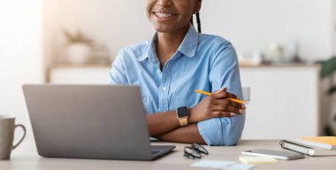 Öğrenciler için çalışmak. Genç siyahi bayan ofis çalışanı pozu dizüstü bilgisayarla masada oturuyor ve kameraya gülümsüyor genç stajyer yeni işin tadını çıkarıyor, boşluğu kopyalıyor.