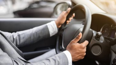 Gümüş takım elbiseli tanınmayan siyahi iş adamının yakın çekimi. Afrikalı Amerikalı girişimci kendi arabasıyla iş toplantısına gidiyor. İki elini de direksiyonda tutuyor.