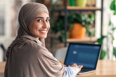tesettürlü gülümseyen müslüman bayanın kafeteryada çalışırken ya da çalışırken, dizüstü bilgisayar kullanırken, kopyalama alanı kullanırken. Türbanlı mutlu Arap kadın dizüstü bilgisayarda yazı yazıyor, uzak işinden zevk alıyor.