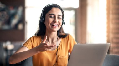 Arkadaşlarıyla sohbet eden, kulaklık ve dizüstü bilgisayar kullanan, uzaydan kopya çeken genç bir kadın.