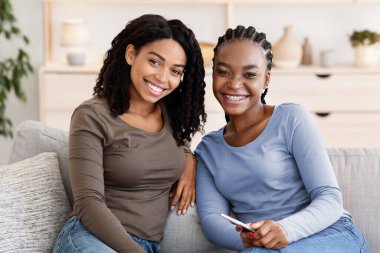 Mutlu Afrikalı kadınlar evdeki kanepede oturup kameraya gülümsüyorlar.