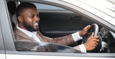 Takım elbiseli Afro-Amerikan genç adam yola bakıyor ve gülümsüyor. Lüks beyaz arabasıyla ofise giden mutlu siyah işadamı iş toplantısını düşünüyor.