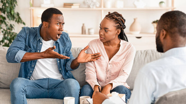 Беспокойный черный мужчина жалуется на проблемы в отношениях с женой в офисе семейного консультанта, эмоционально делится историей, психотерапевт слушает информацию