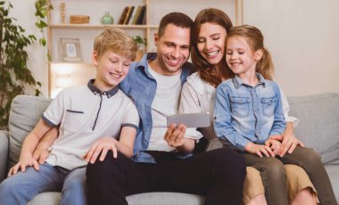 Dört kişilik bir aile cep telefonu kullanıyor, birlikte çizgi film izliyorlar evde koltukta oturuyorlar. Hafta sonu Tatili