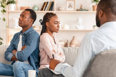 İlişki Krizi. Siyahi erkek ve kadını evlilik danışmanlığı bürosunda sırt sırta oturarak, birbirlerini görmezden gelerek, özgürce oturarak gücendirdiler.