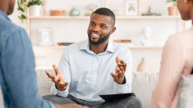 Kendine güvenen siyah aile danışmanı evli bir çiftle konuşuyor, ofisinde tavsiyeler veriyor, seçici bir şekilde boş alana odaklanıyor.