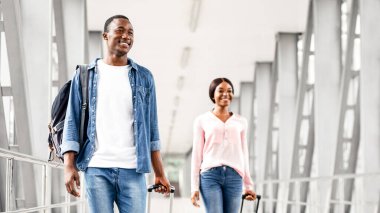 Havalimanı terminalinde bavullarla yürüyen mutlu siyahların portresi, bavulları taşıyan Afrikalı Amerikalı erkek ve kadın, uçuş kapısına gidiyor, tatil gezisi için hazır, bedava uzay...