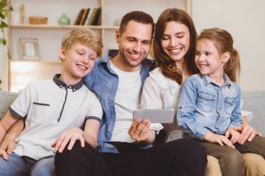 Neşeli aile, hafta sonları evdeki koltukta oturup interneti birlikte gezerek akıllı telefon kullanıyor. Mobil Uygulama Kavramı