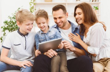 Neşeli bir aile tablet bilgisayar kullanıyor, birlikte zaman geçiriyorlar, koltukta oturuyorlar ve çizgi film izliyorlar. Hafta Sonu Evde.