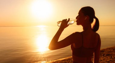 İşten sonra su içen güzel atlet kadın silueti yaz akşamları sahilde egzersiz yapıyor.