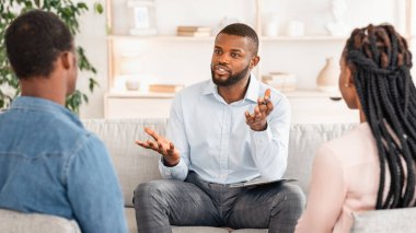 Aile psikoterapisi. Ofisteki terapi sırasında danışman danışmanı dinleyen Afrikalı Amerikalı çift, Siyahi Eşler Terapist ve Seçici Odaklanma ile Evlilik Danışmanlığı Toplantısı yapıyor