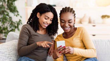 Neşeli Afrikalı kız arkadaşlar akıllı telefondan fotoğraf izliyorlar, ev içi, yakın plan