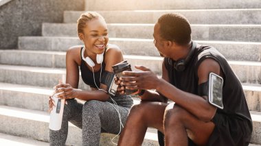 Siyah çift dışarıda idman yaptıktan sonra dinleniyor, şehir merdivenlerinde oturuyor, su içiyor, kahve içiyor, sohbet ediyor, boş bir alanda takılıyor.