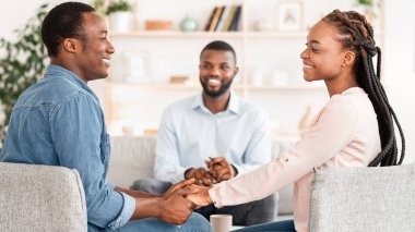 Evliliği kurtardım. Mutlu Afrikalı eşler uzlaşmadan sonra danışmanlık bürosunda el ele tutuşuyor, birbirlerine bakıyor ve gülümsüyorlar.