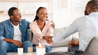 Başarılı bir evlilik terapisi. Uzlaşmadan sonra aile danışmanıyla tokalaşan mutlu siyah eşler, mesleki yardım ve kurtarılmış evlilik için şükranlar, ofisteki koltukta oturma, boş yer.