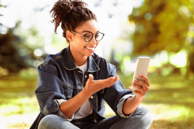 Açık havada oturan uzak bir arkadaşıyla telefonda görüntülü konuşma yapan siyahi bir kız. Modern İletişim. Seçici Odaklanma